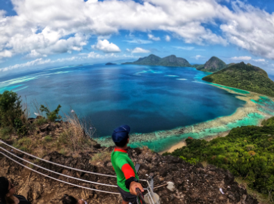 A man holding up the camera to show the view of the ocean at Bohey Dulang trekking trail on a sunny day