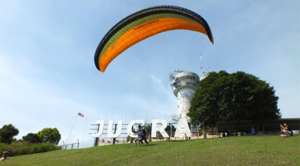 A paraglider taking off in front of a "Jugra" sign on a sunny day