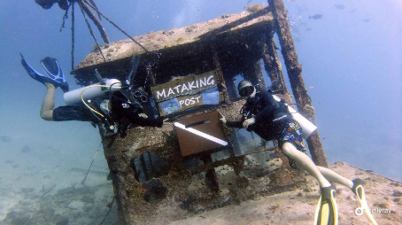 Two divers posing with an underwater shack with a signboard saying "Mataking Post"