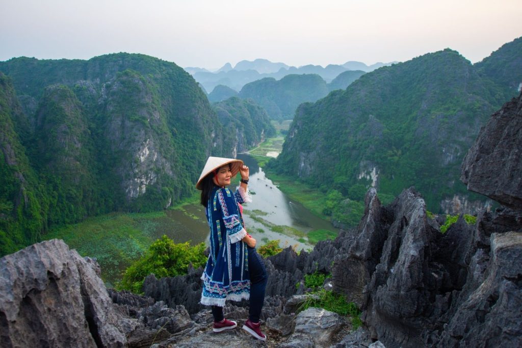 A woman stands on a jagged limestone peak at Mua Caves in Ninh Binh, Vietnam. Highlight vietnam travel budget